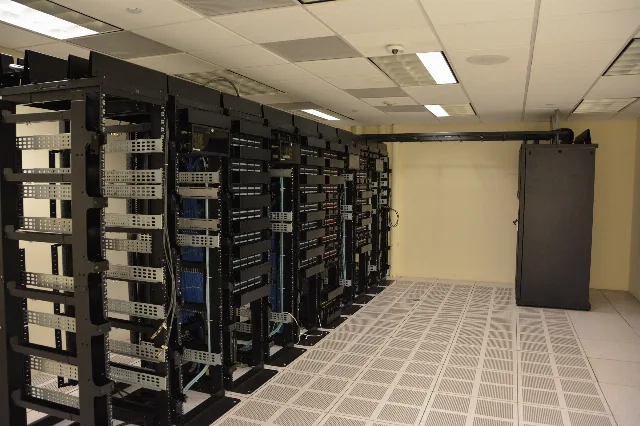 Fileiras de racks de servidores pretos, com cabos azuis, em um data center de piso elevado