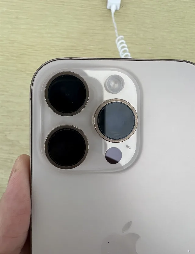 Traseira de um iPhone 16 Pro dourado, com o conjunto de três câmeras, segurado por uma mão