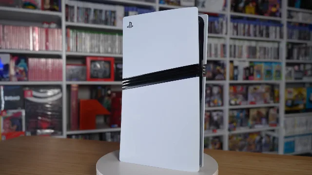 Console PlayStation 5 Pro branco, em pé, com as faixas pretas no meio, diante de uma estante de jogos